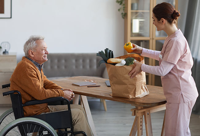 nurse helping older man in wheelchair with his groceries